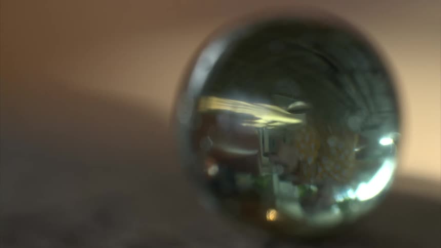 A close up of a marble reflecting a girl about to pick it up
