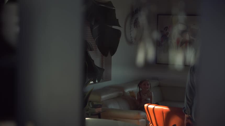A girl is sitting on the couch through the window