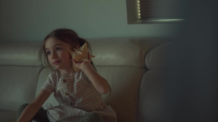 A girl is listening to a sea shell by her ear