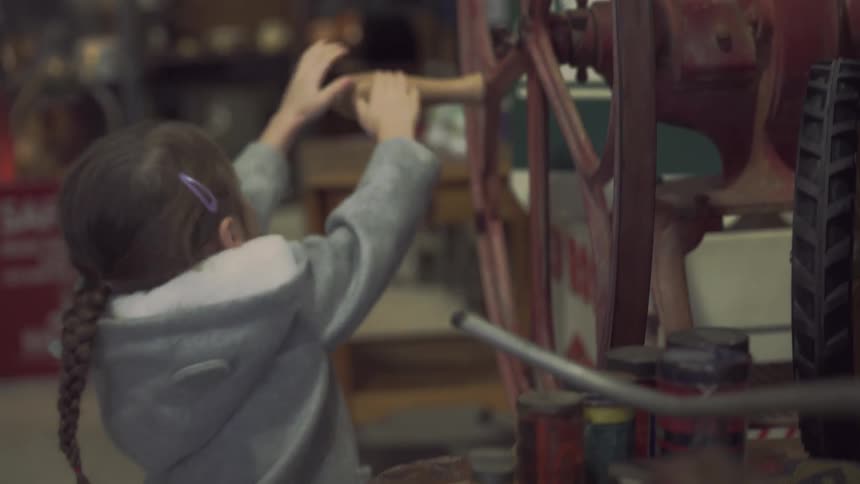 A little girl plays with a wheel of an old machine in a store