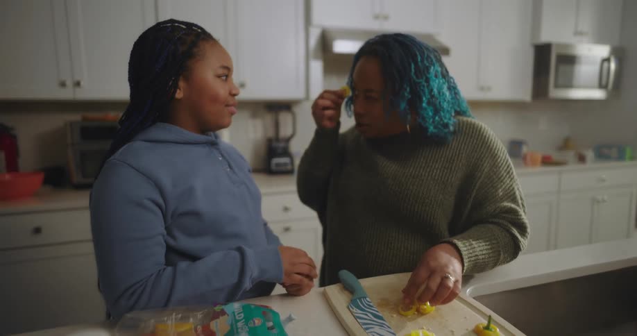 Mother feeds her daughter a vegetable slice while cooking in the kitchen on an autumn day