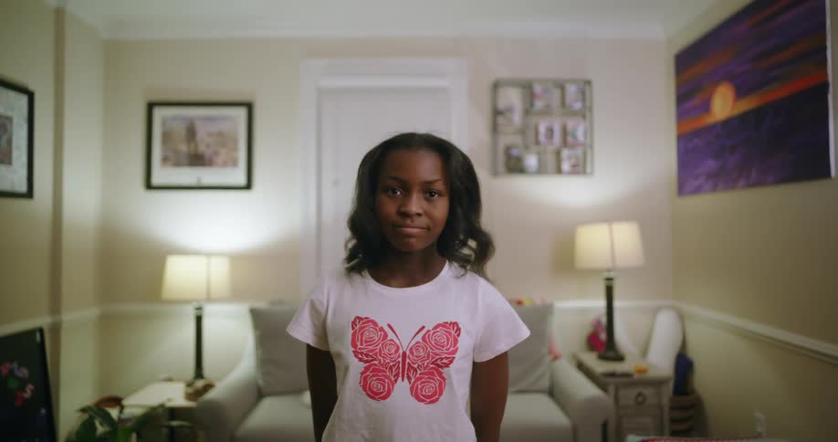 A girl wearing a white shirt with a pink butterfly stands on a modern living room