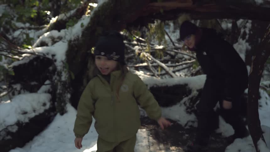 Mother and daughter wearing thick winter clothes walk around fallen trees on a snow covered forest