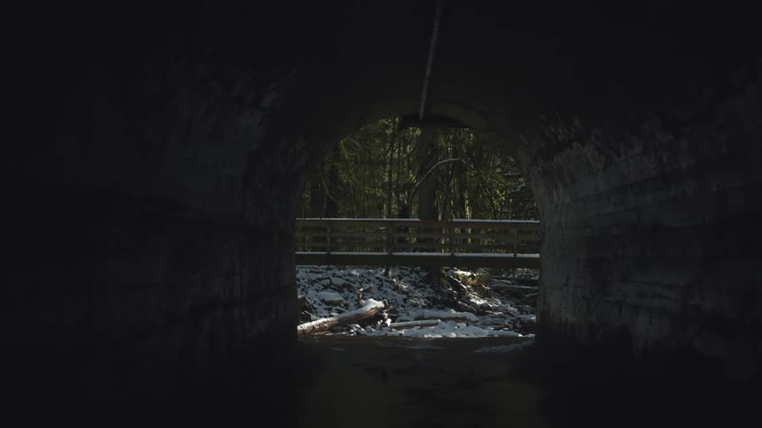 Two people cross a bridge passing over the creek flowing through a nearby tunnel
