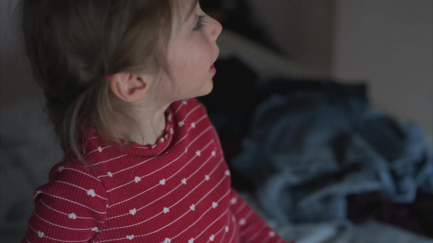 A little girl smiles and plays as her mom folds clothes and hands them to her