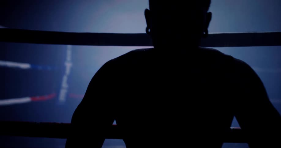 A boxer is sitting on the ring wiping sweat from his face