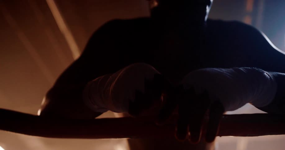 A boxer is leaning against the ropes of a ring