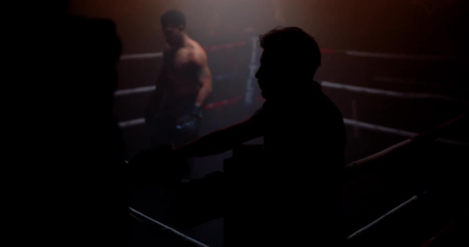 Boxer bounces on his feet while in a boxing ring in a dimly lit area