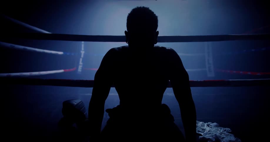 A dramatic silhouette of a boxer sitting in the ring illuminated by moody lighting conveying exhaustion and determination