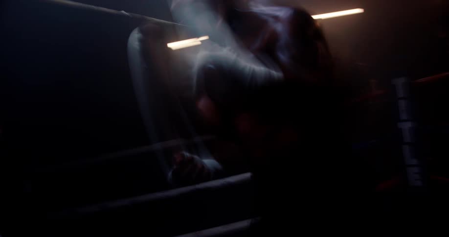 A man is shadowboxing in the dark ring