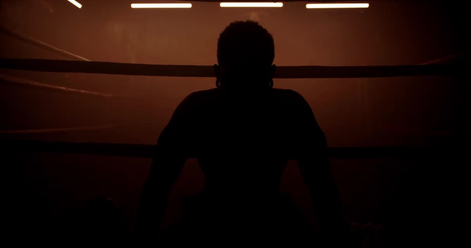 Silhouette of a man sitting outside a boxing ring in a lowlight environment