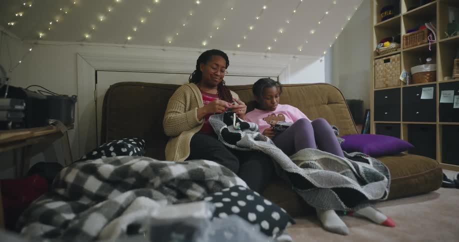 Mother sitting on a sofa next to her daughter while knitting