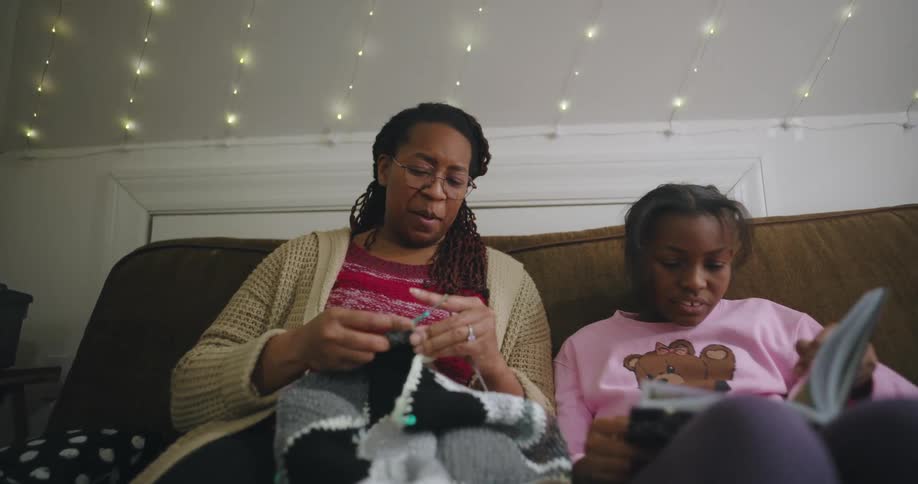 Mother knitting while sitting next to her daughter who is reading a book