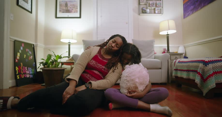 Mother and daughter sitting on a wooden floor in a modern living room leaning against each other