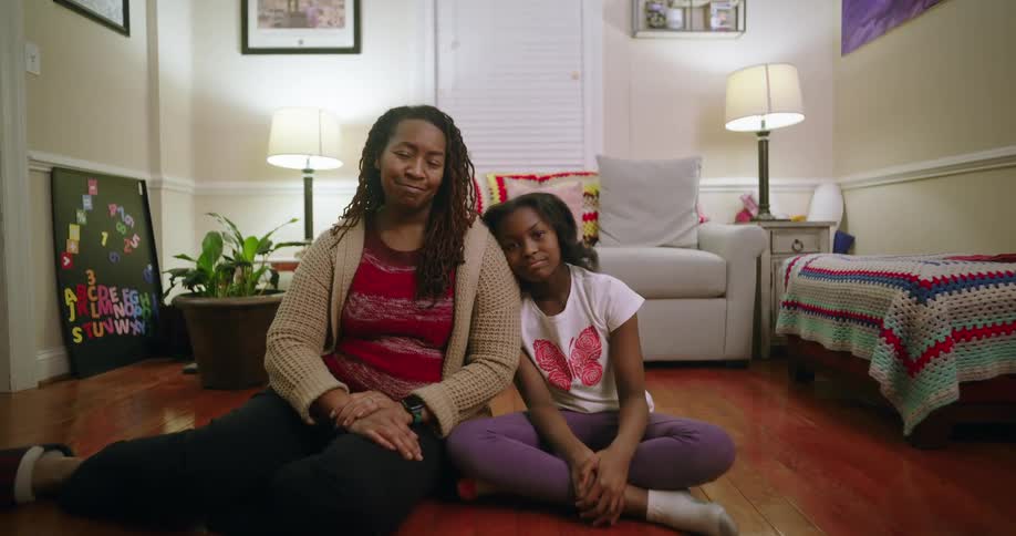 A mother and daughter sit close together on the floor of a modern living room