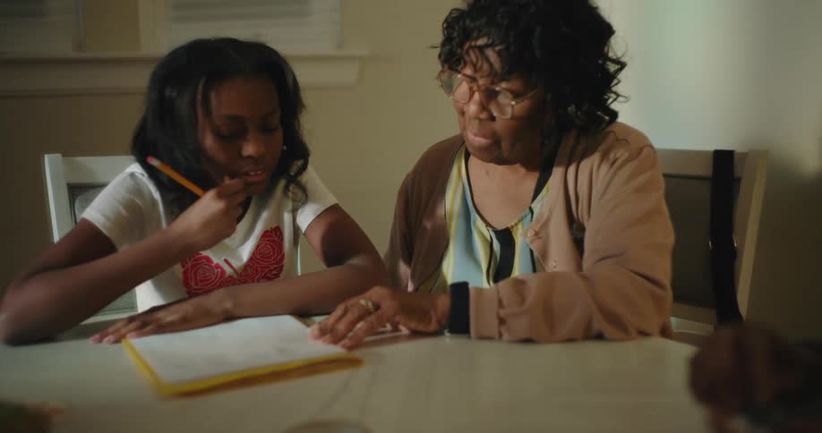 A grandmother watches while her granddaughter explains her schoolwork