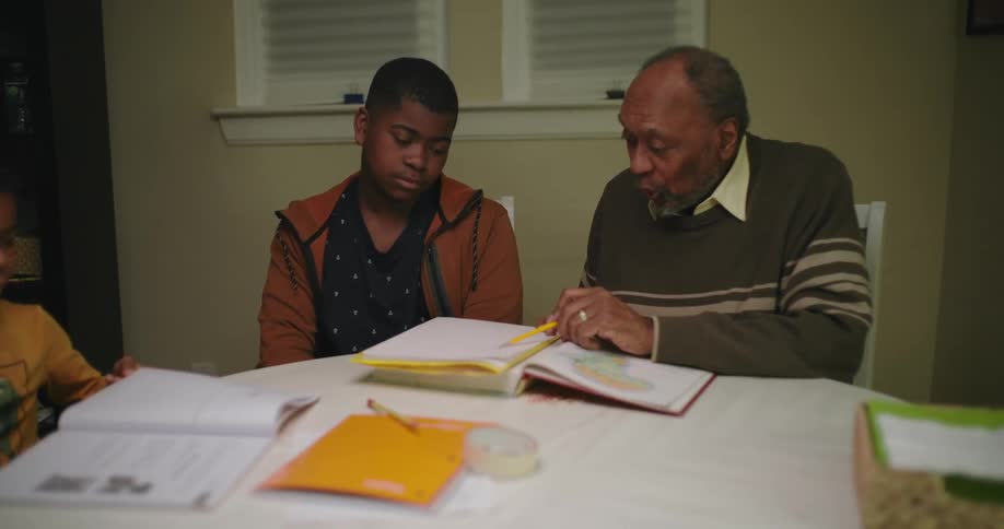 A man helps a boy with his homework at a table in a house