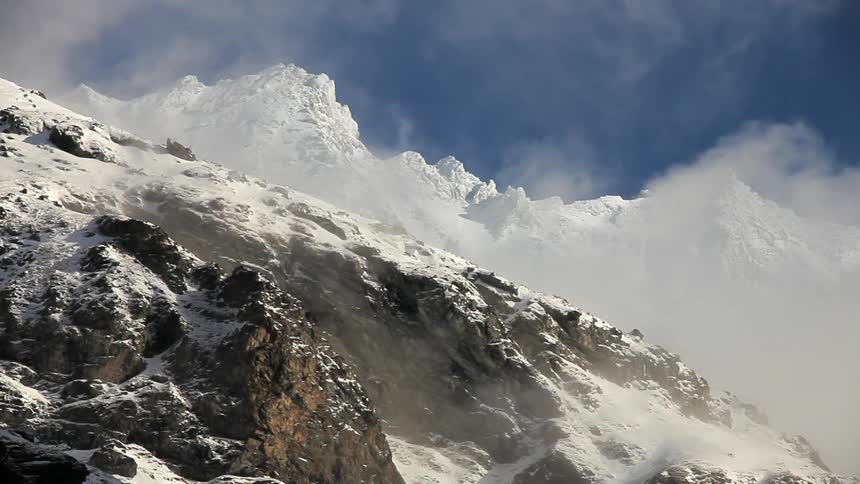 Wisps of clouds hover amidst snow-covered mountains