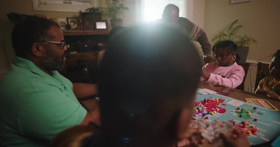 Family having fun playing board game in dining room as grandfather looks on
