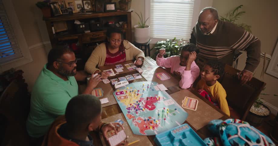 Family sitting around dining table playing a board game as grandfather watches