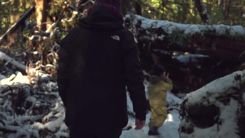 Child followed by an adult walking in the middle of a snowy forest
