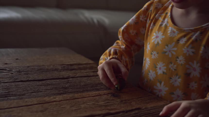 A girl in a yellow dress plays with a marble on a rustic table in the living room