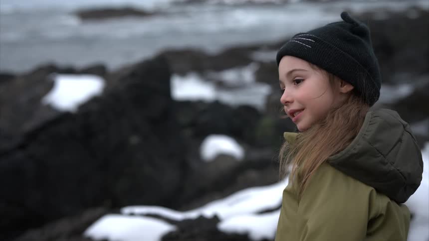Little girl in a black cap among rocks by the sea
