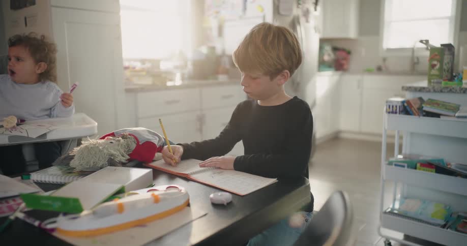 A boy works on his homework at the dining table situated near the kitchen in his home