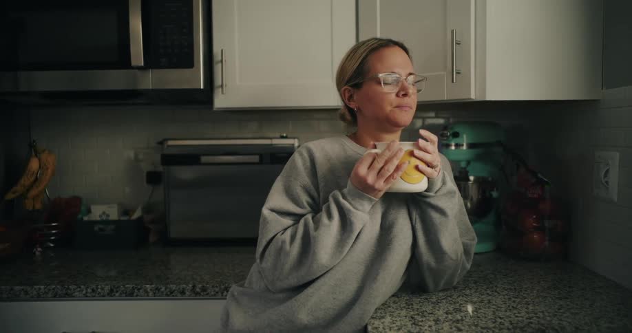 Woman in kitchen taking a deep breath and holding a mug