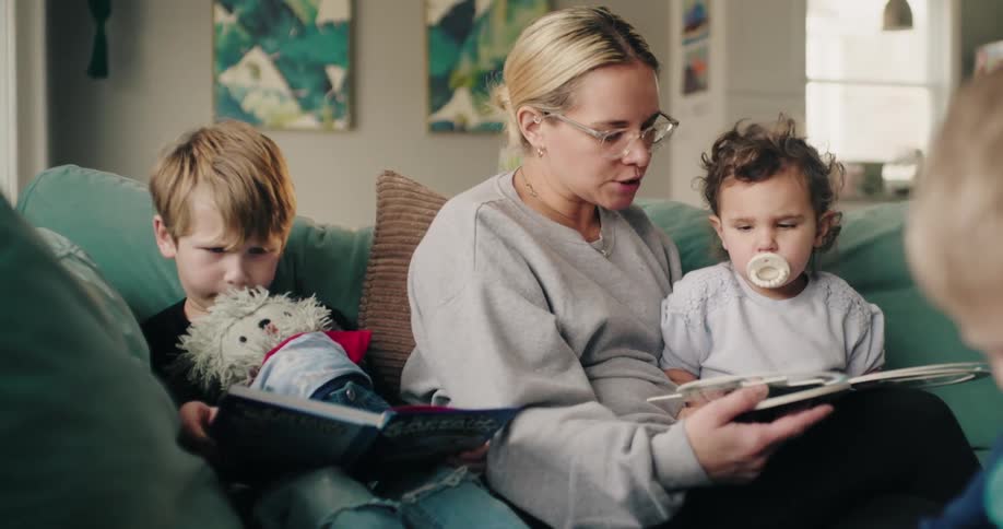 A busy mother sitting on a couch at home reading with her children