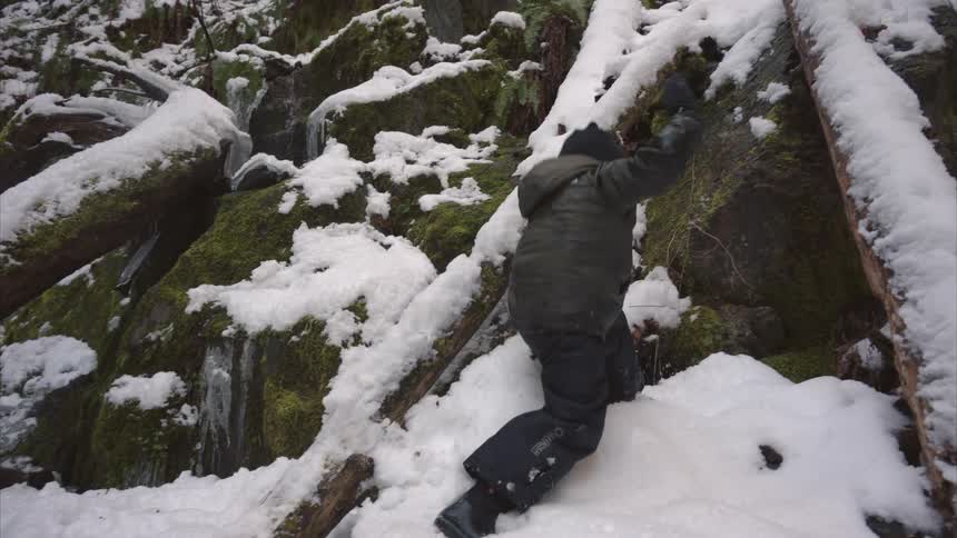 Child climbs up a snowy slope strewn with fallen trees