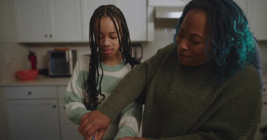 Family prepares food together in the kitchen with the daughter cutting vegetables under her mothers guidance