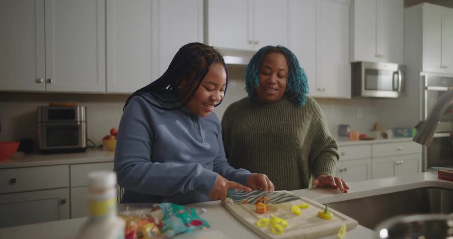 A woman with blue hair and a teenager chopping vegetables on the kitchen at home