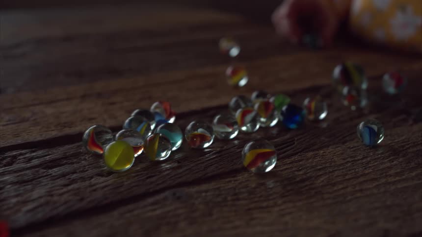 A childs hand reaches for scattered marbles on a weathered wooden surface