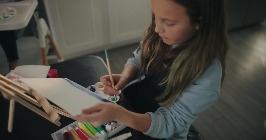 A girl sitting on a table at home painting with oils