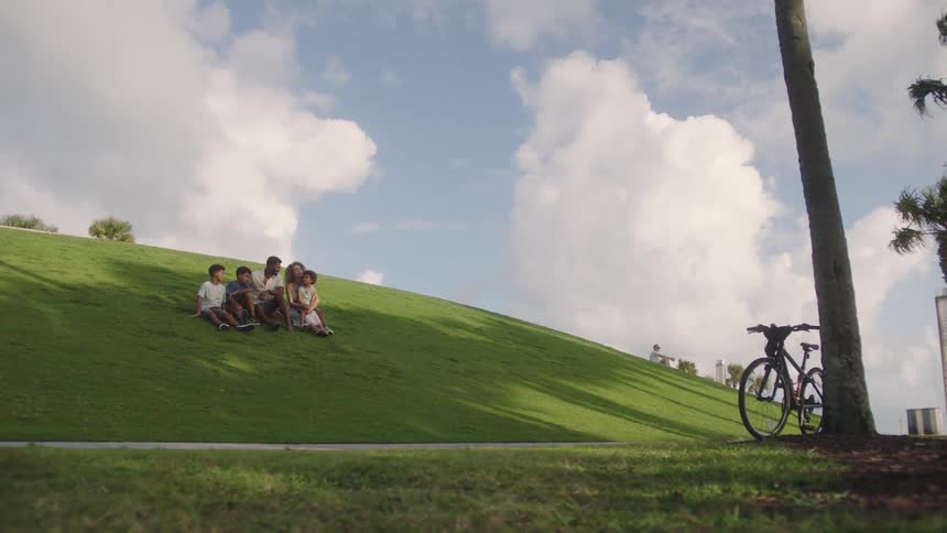 A family sits in the grass on a hill at a park
