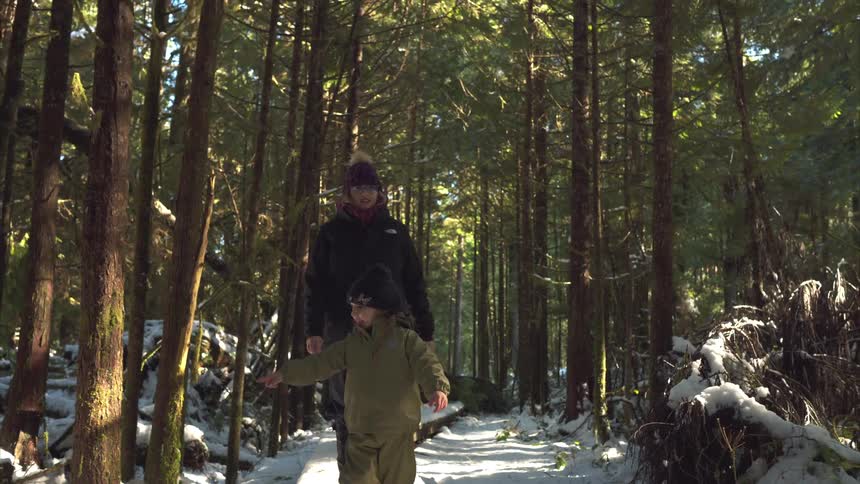Daughter smiles while she and her mother walk through the woods on a winter day