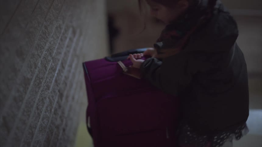 A child drags her luggage up the stairs