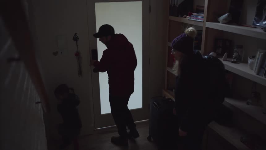 A family carrying luggage arrives home after a vacation trip