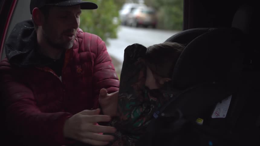 A father secures his daughter in a child seat on the passenger side of a van