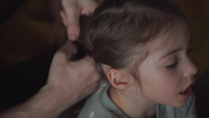 Girl talks while her father braids her hair