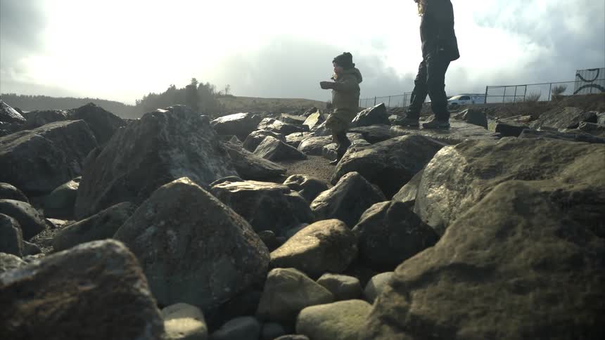 A mother and daughter climb over the large rocks on the shore