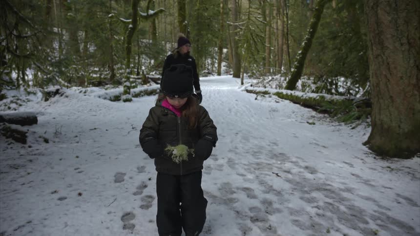 Little girl walking in the snow accompanied by an adult and trees around