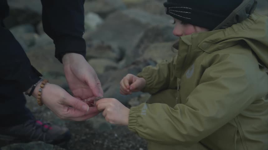 Mother hands a shell to a girl so the child can listen to it while they explore during the day