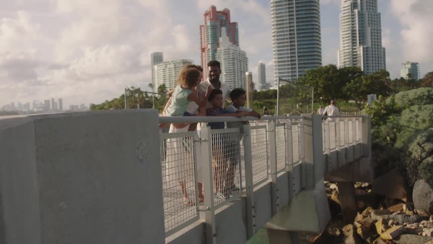 The family of five is standing on the white bridge and behind them is large sky scrappers