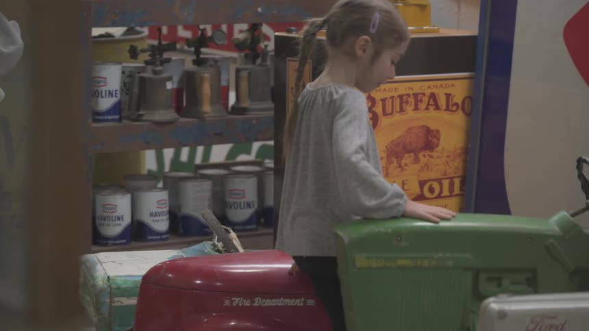 A girl playing with life size vintage toy cars on a store