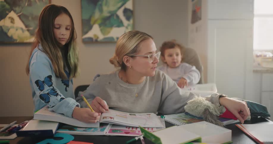 A mother helps her children with their homework at the dining table in their home