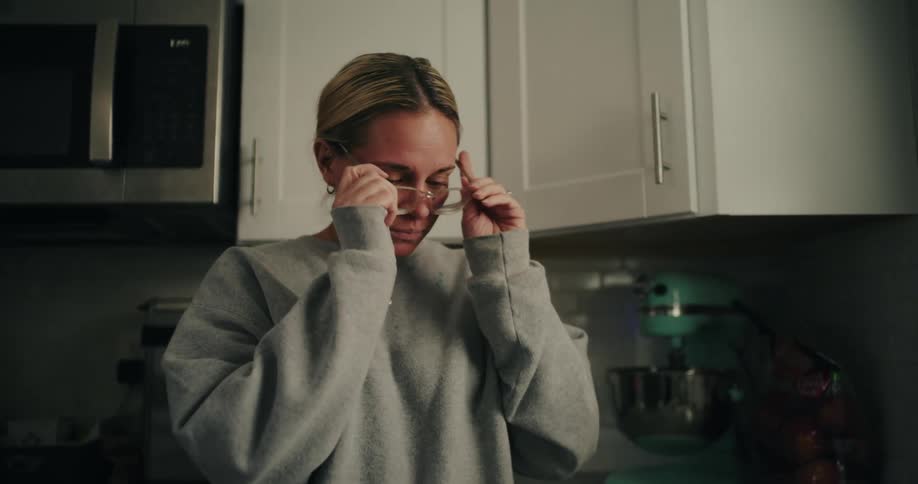 A woman puts on her glasses and picks up a cup of coffee