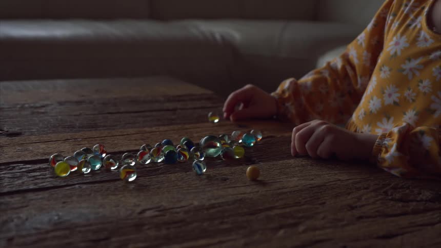 Girl plays with marbles on the wooden table in the living room during the day