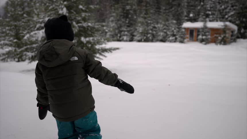 Child walks through the snow with a house and trees in the background